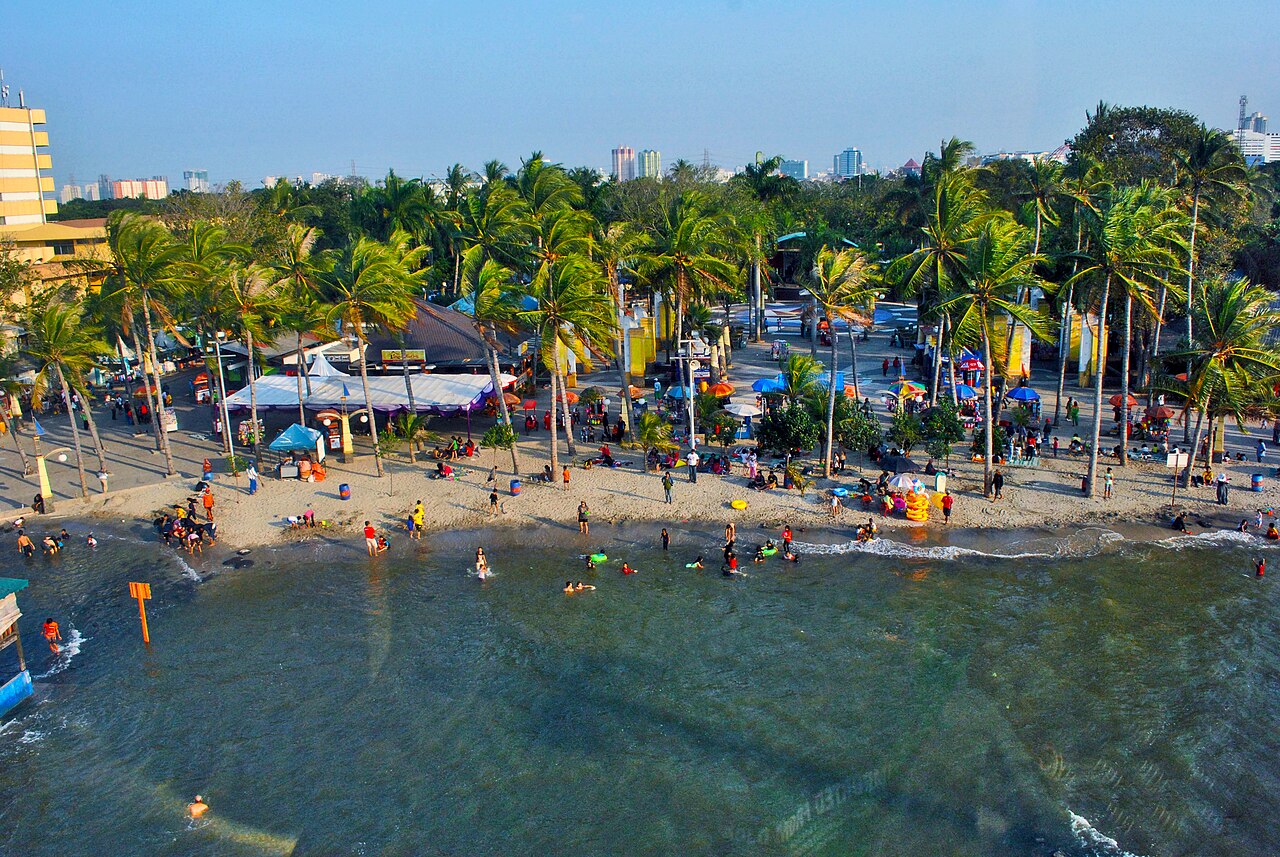 Pemandangan pengunjung di Pantai Ancol dengan deretan pohon kelapa